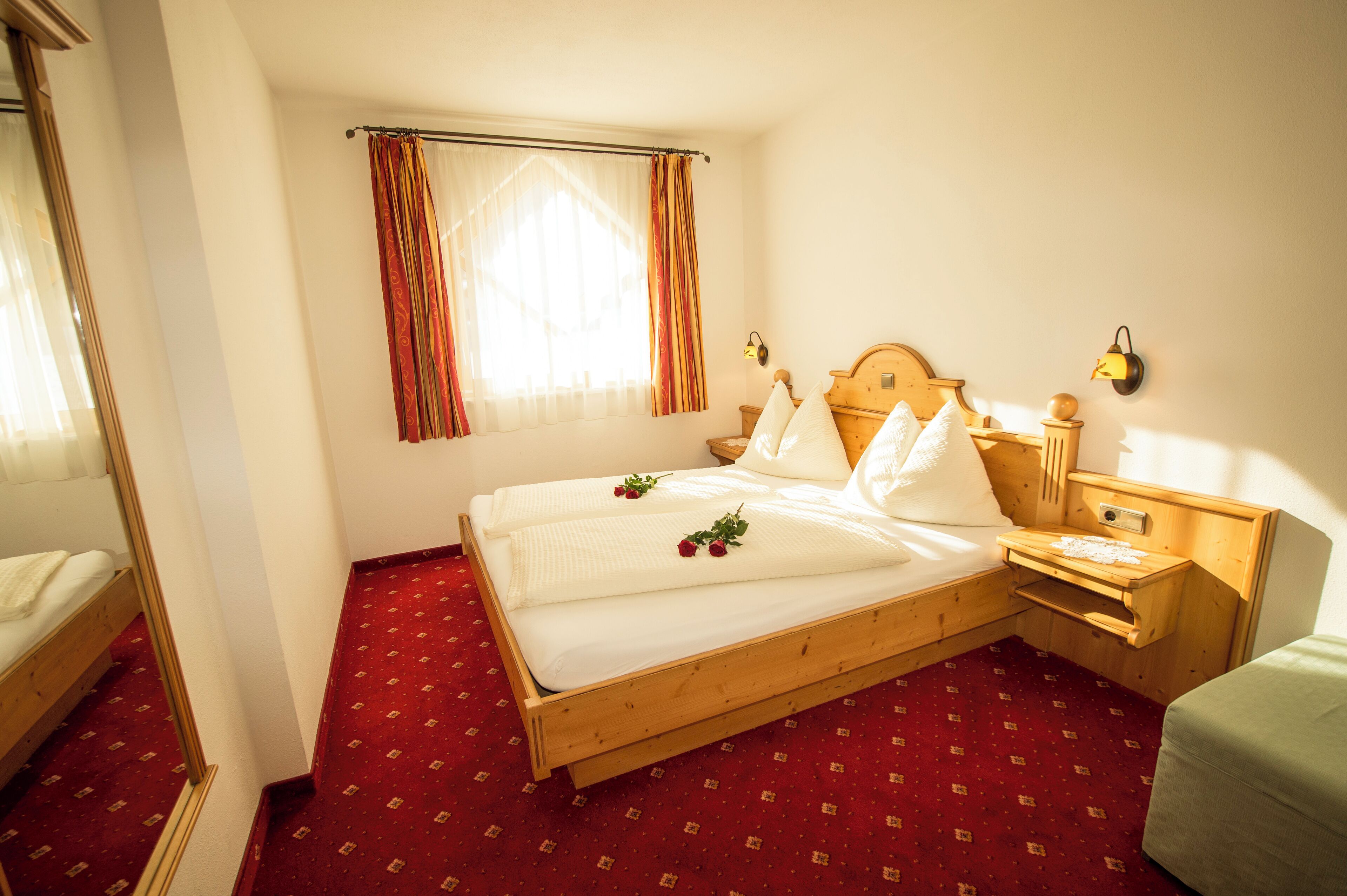 A wooden bed with white linens, a nightstand with a lamp, and a red carpeted floor.