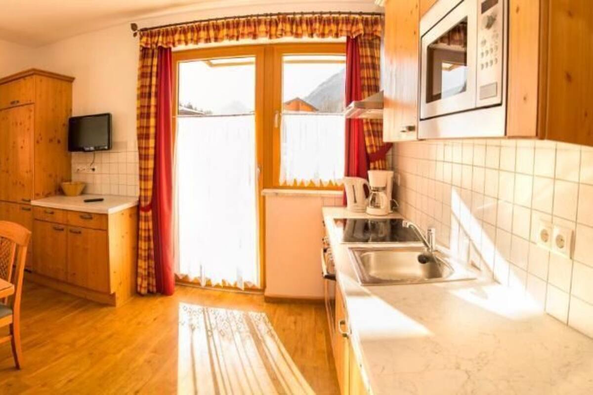 A cozy kitchen with a wooden table and chairs, a built-in oven, and a window with curtains.