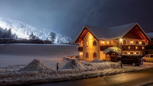 A snow-covered lodge with a warm-lit entrance and a view of a snowy mountain in the background. - Flachauer Bergkristall (Flachau)