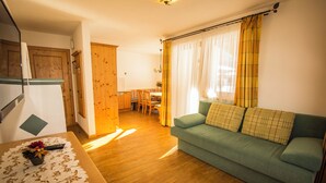 A cozy living room with a green sofa, wooden flooring, and a dining area with a table and chairs. - Flachauer Bergkristall (Flachau)