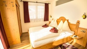 A wooden bed with white linens, a bedside table, and a window with curtains. - Flachauer Bergkristall (Flachau)