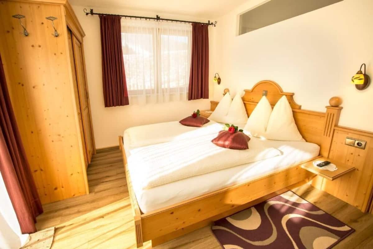 A wooden bed with white linens, a bedside table, and a window with curtains.