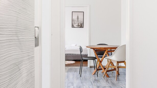 Una habitación de hotel moderna con una mesa de comedor de madera, dos sillas, un cuadro enmarcado en la pared y una puerta blanca con textura.