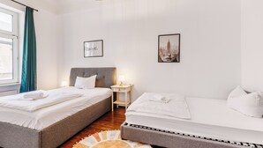Una habitación de hotel moderna con dos camas, una mesita de noche pequeña con una lámpara, y un cuadro de paisaje urbano en la pared.