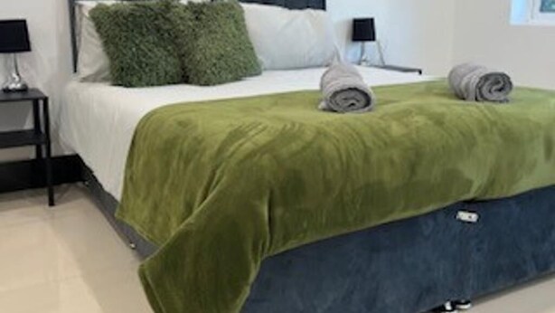 A bedroom with a bed, green and blue bedding, two pillows, a nightstand with a lamp, and a window. - Urban, Sleeps 6 Private Garden-family Pet Friendly (Croydon)