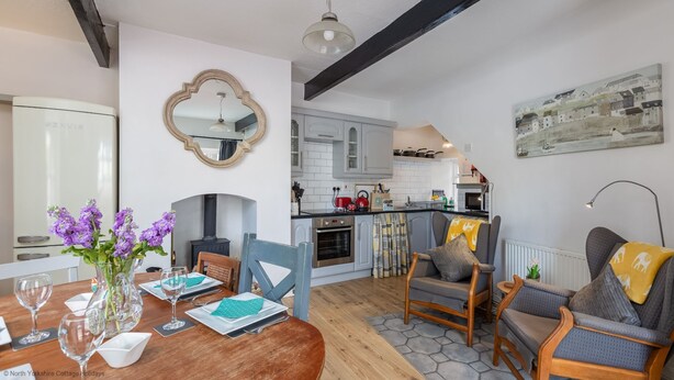 A dining area with a wooden table set for four, a vase with purple flowers, and a mirror on the wall. - Grade II Quirky Yorkshire Cottage (ADDINGHAM)