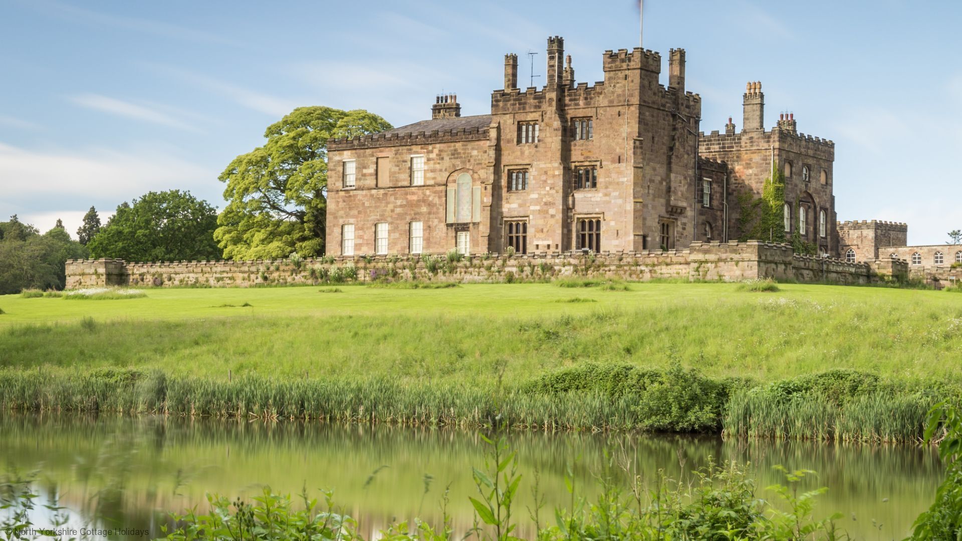 A historic stone castle with multiple towers and a large lawn in front.