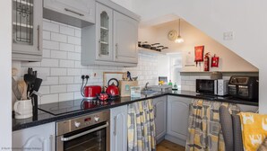 A modern kitchen with white cabinetry, a built-in oven, a red kettle, and a microwave. - Grade II Quirky Yorkshire Cottage (ADDINGHAM)