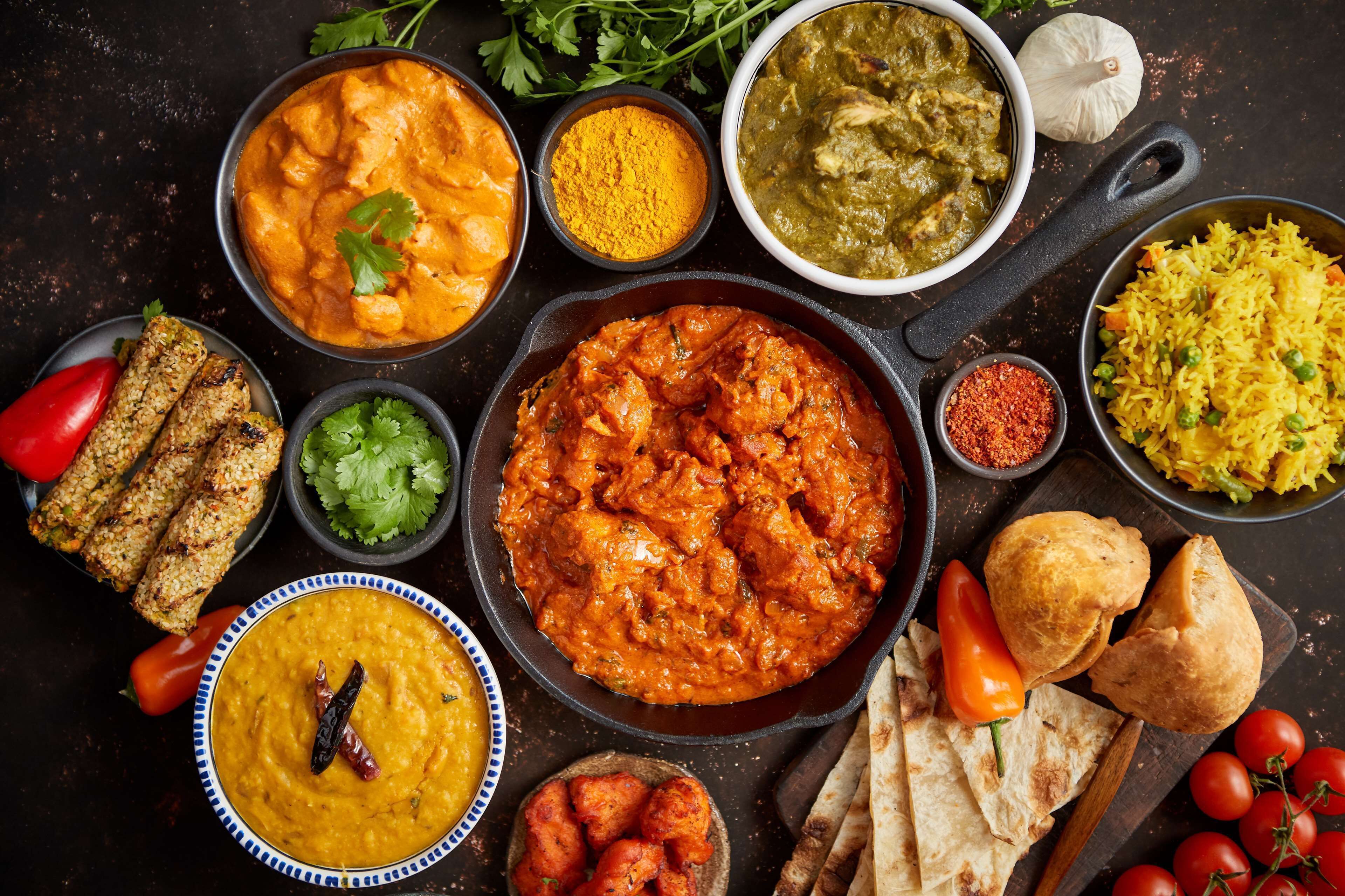 A variety of Indian dishes including curries and rice, accompanied by bread and vegetables.