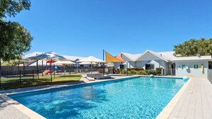 A swimming pool with a fenced play area, shaded seating, and a building with a white roof. - By the Sea at Cape View Resort (Broadwater)