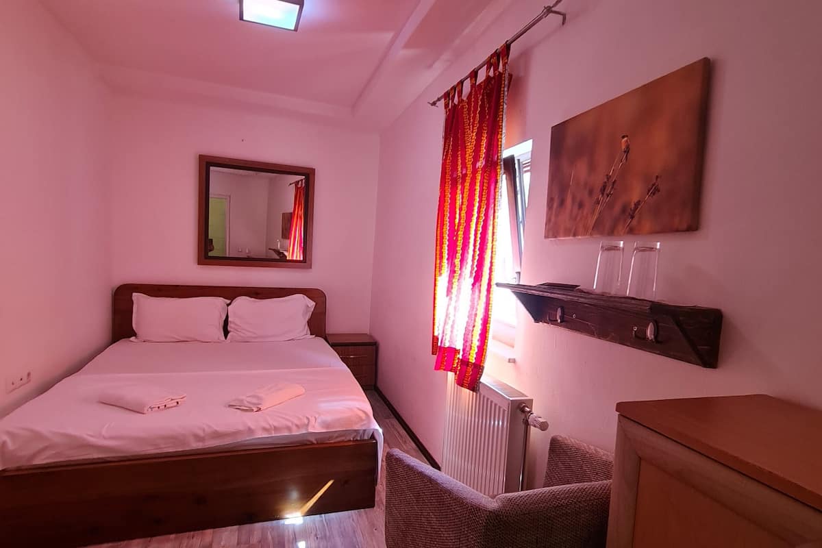 Ein Schlafzimmer mit einem großen Bett, einem Sessel, einem Holzschrank, einer Heizung, einem Spiegel und einem Bild an der Wand.