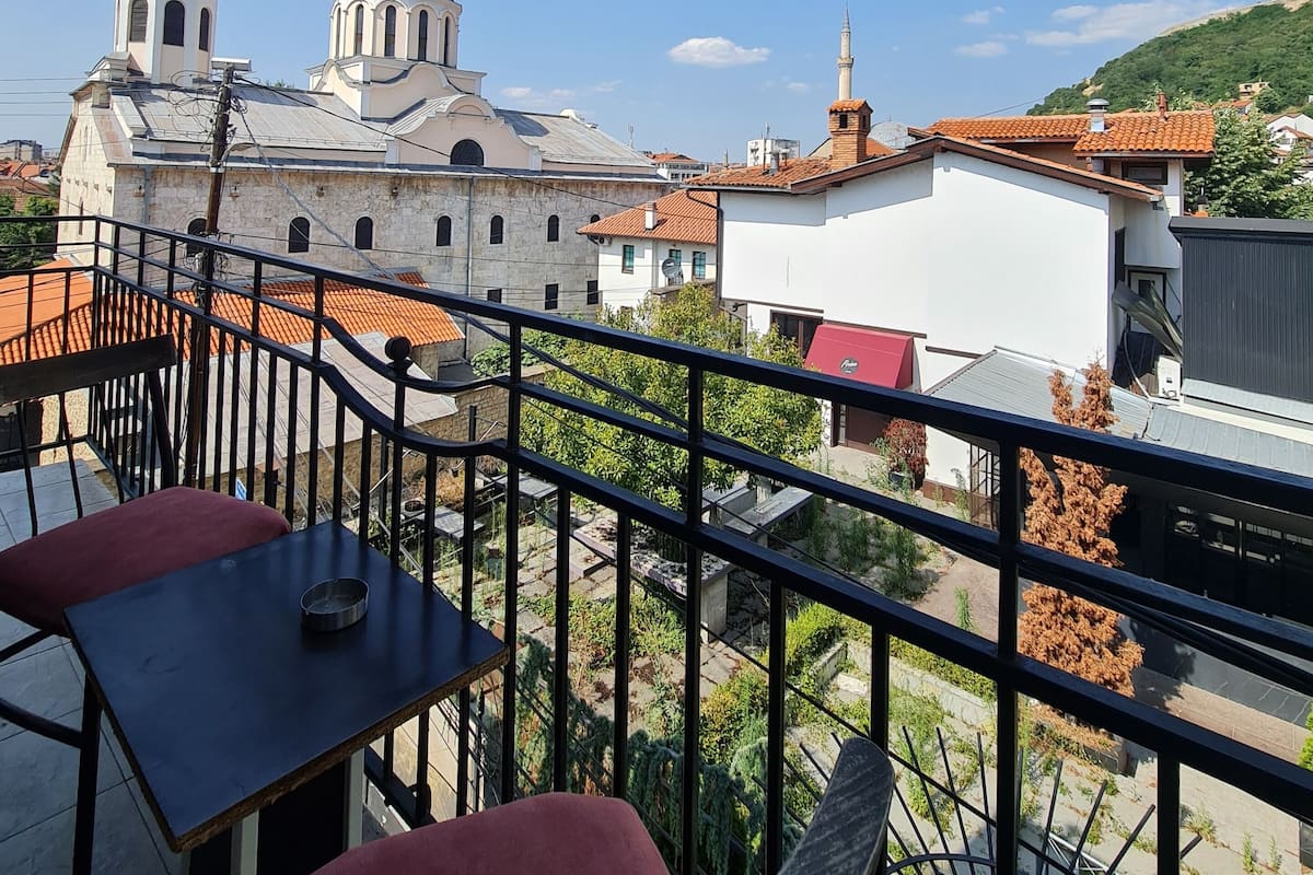 Ein Balkon mit Blick auf ein historisches Gebäude mit Kuppeln und einem Minarett, umgeben von moderner Bebauung und Grünflächen.