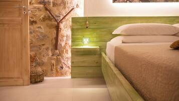 Un dormitorio con pared de piedra, cabecero de madera y cama con ropa blanca.