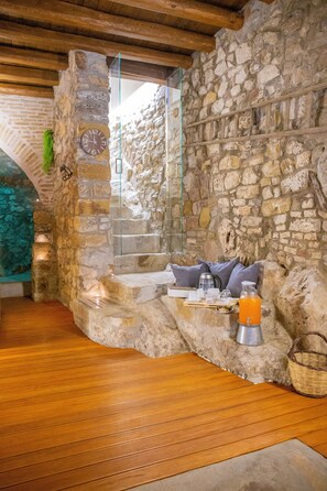 A stone-walled room with a wooden floor, a stone bench with cushions, a glass door, and a clock. - PORTA SOPRANA Luxury guest house &Spa (Sclafani Bagni)