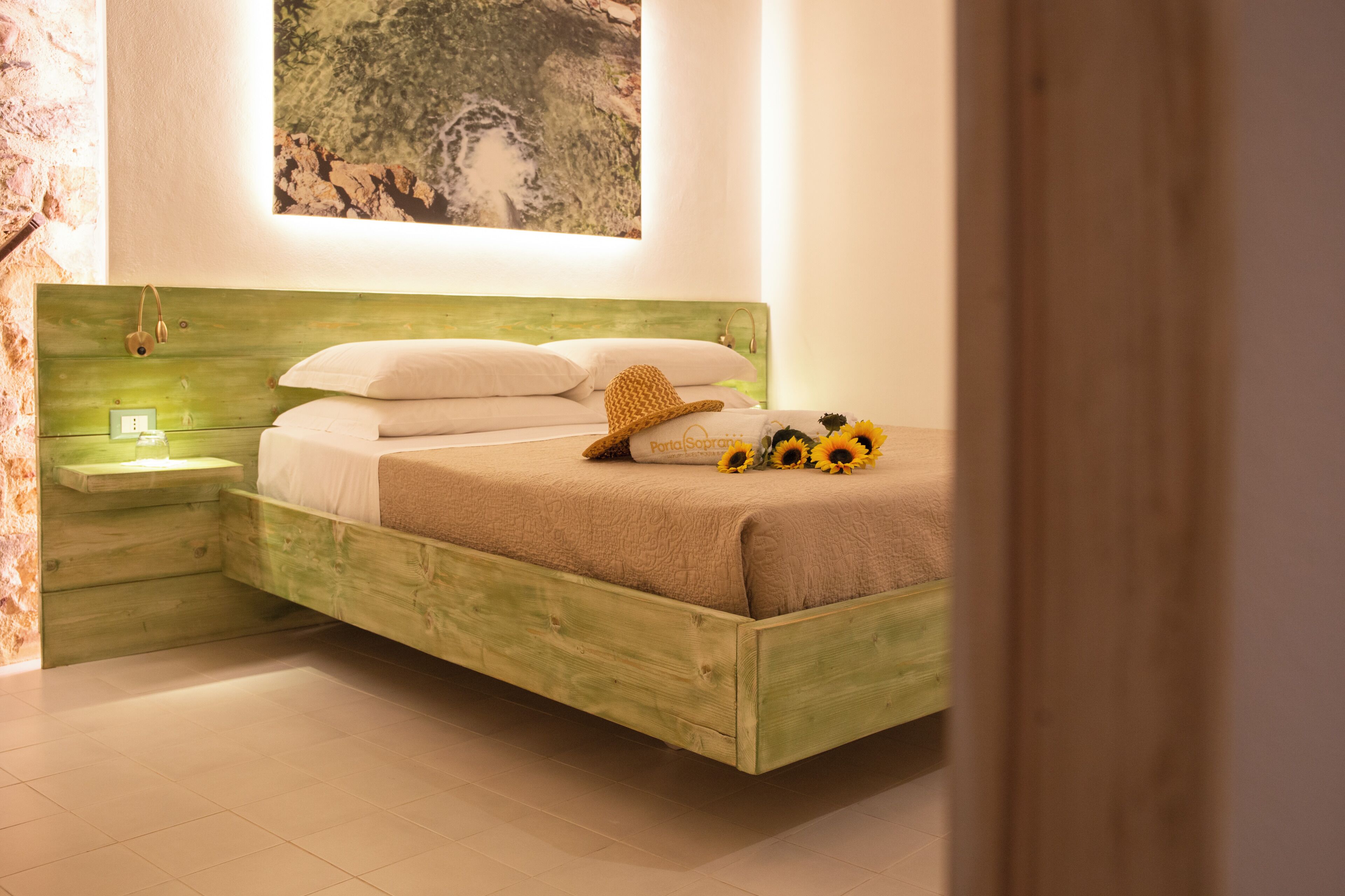 Ein hölzernes Bett mit weißer Bettwäsche, ein Nachttisch und ein an der Wand befestigtes Regal.
