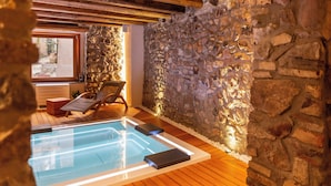 A stone-walled room with a wooden floor, a glass-enclosed pool, and a lounge chair. - PORTA SOPRANA Luxury guest house &Spa (Sclafani Bagni)