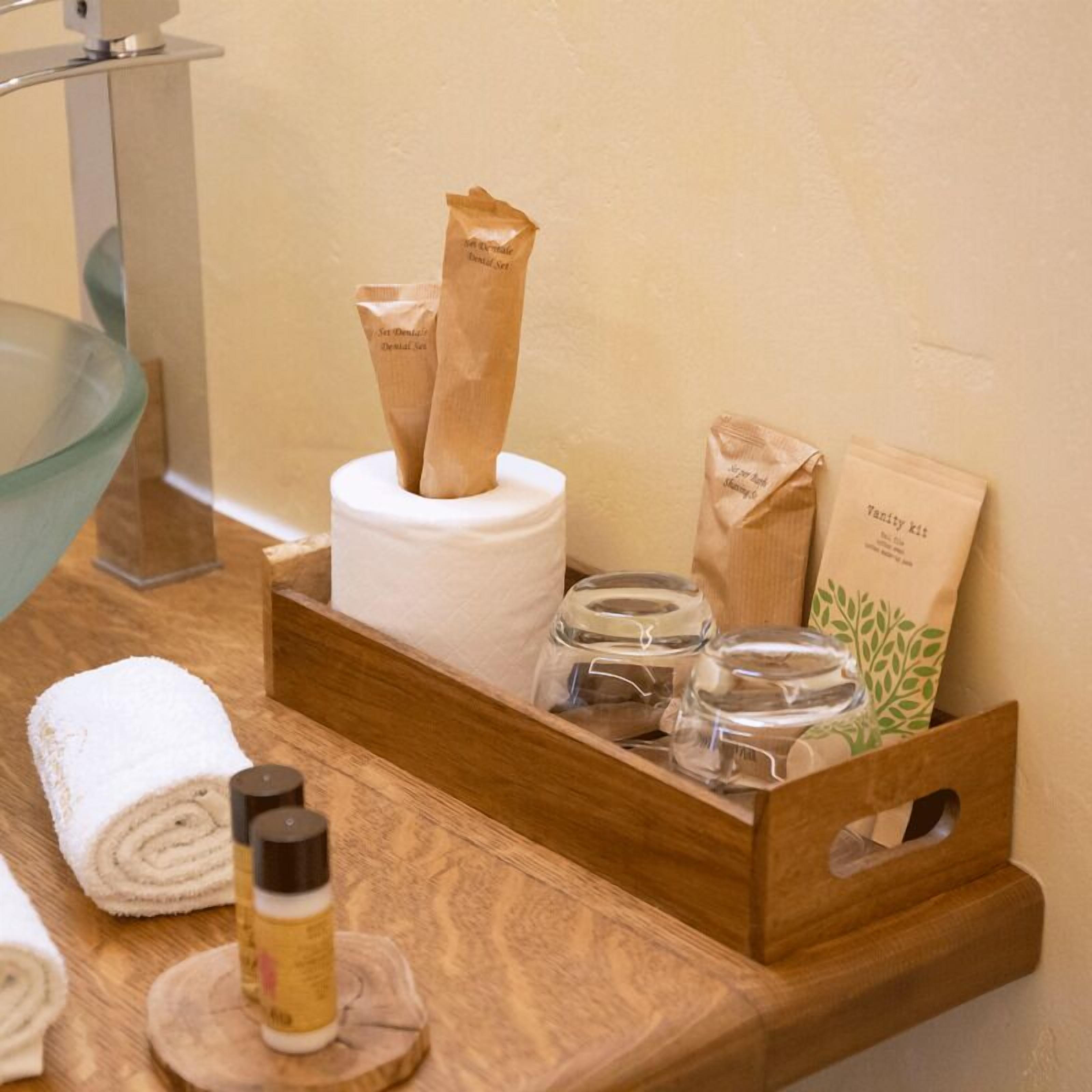 Una bandeja de madera con un rollo de papel higiénico, una botella y dos toallas de papel sobre una encimera de baño.