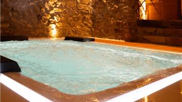 A stone-walled room with a rectangular pool and a wooden bench.