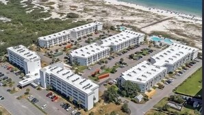 Eine Vogelperspektive auf ein Küstenhotel mit mehreren Gebäuden, Parkplätzen und einem Strand im Hintergrund.