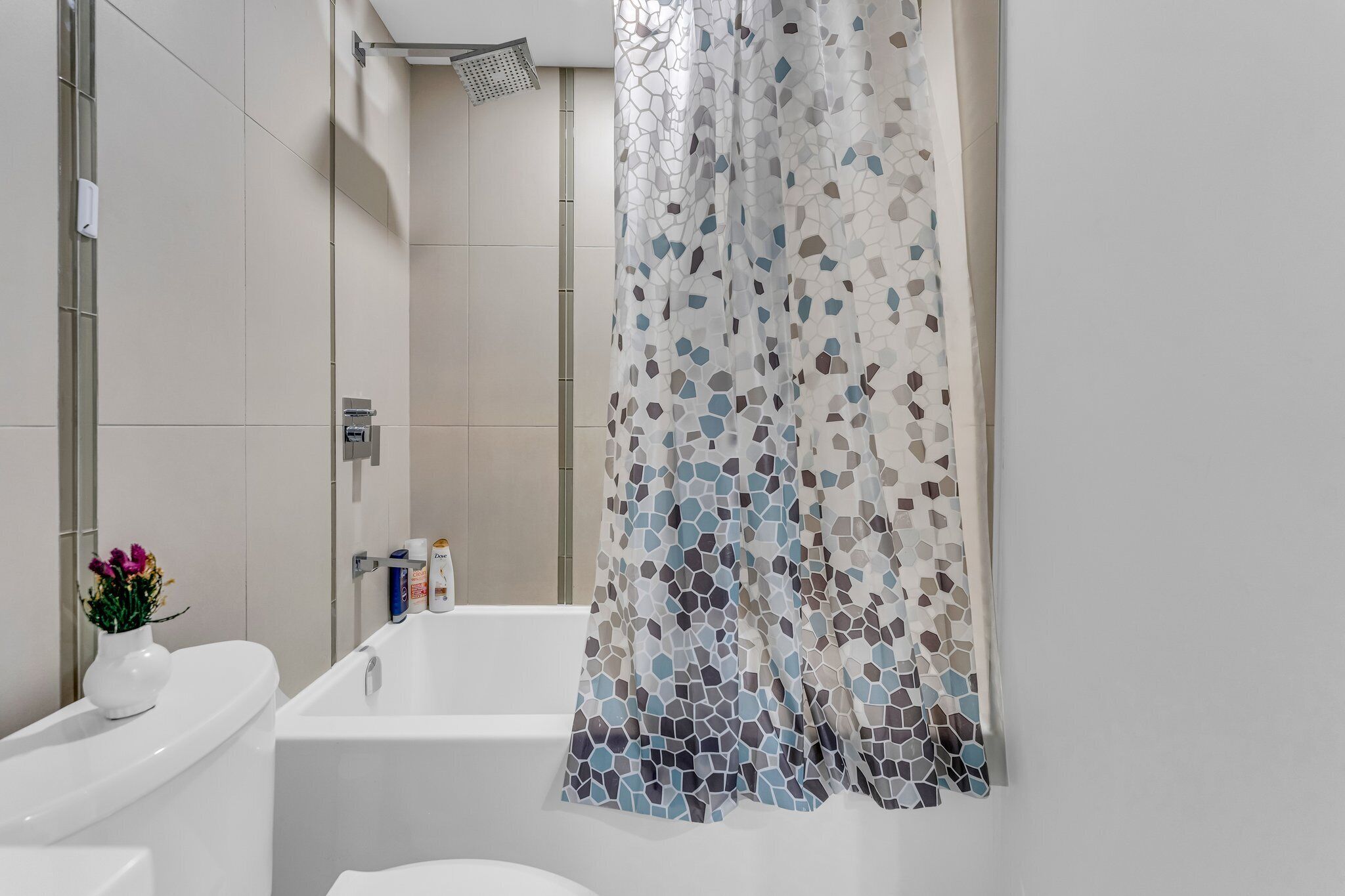 A modern bathroom with a white bathtub, a shower with a rain showerhead, and a mosaic-patterned shower curtain.