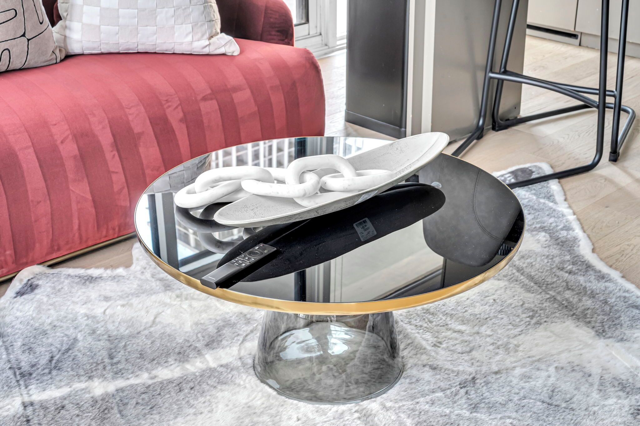 Una mesa redonda de cristal con borde dorado y base negra, que presenta un diseño de cadena blanca sobre la superficie.