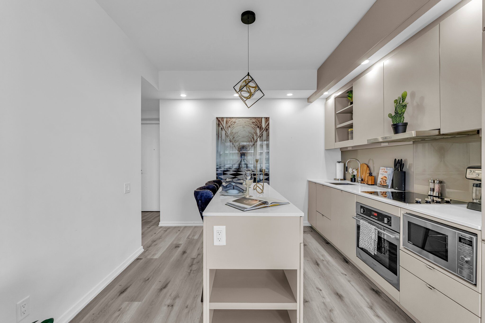 Una cocina moderna con una isla central, horno empotrado, microondas y una lámpara colgante.