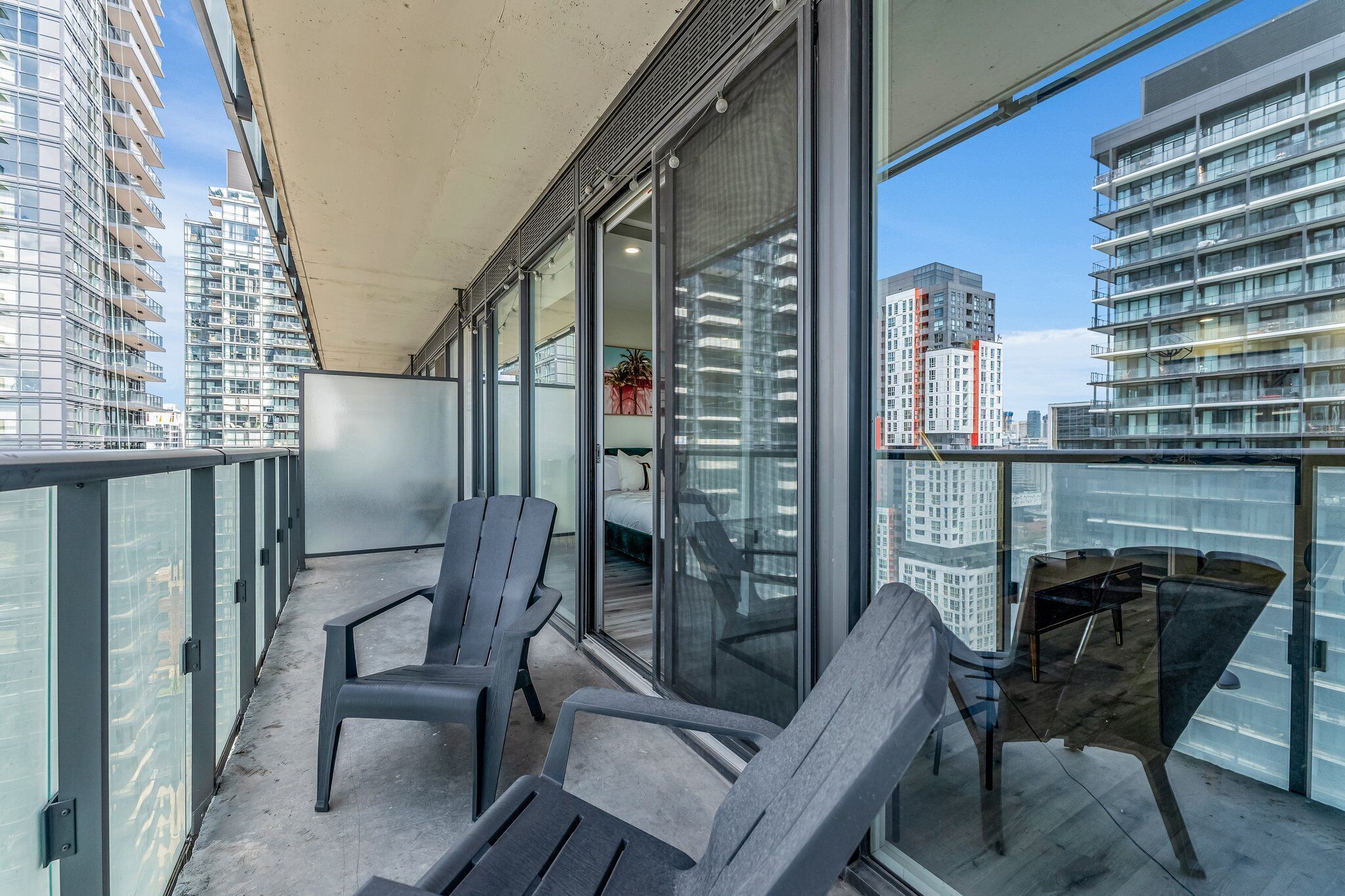 A balcony with two Adirondack chairs, a glass table, and a view of high-rise buildings.