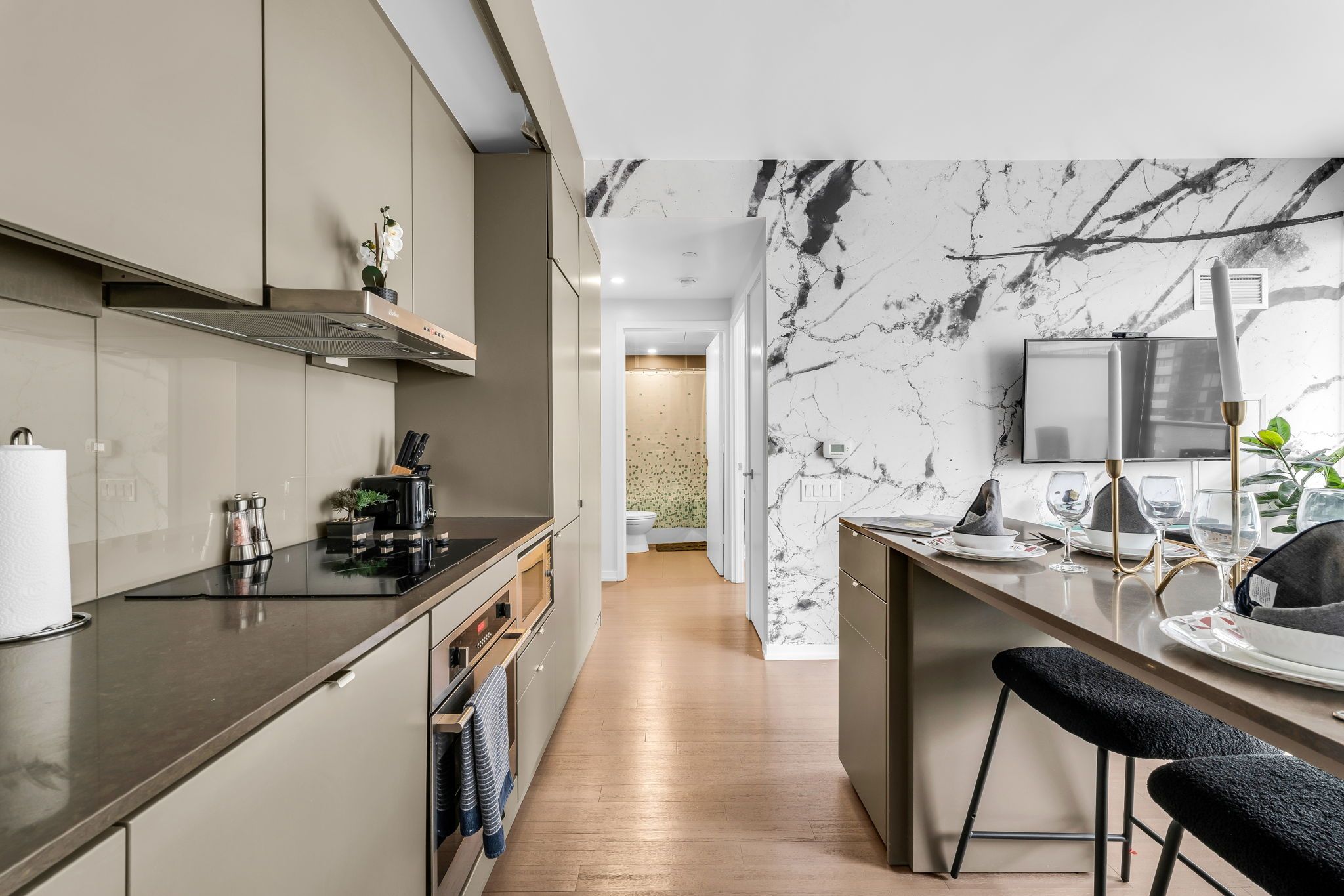 A modern kitchen with a marble backsplash, a built-in oven, and a bar area with stools.