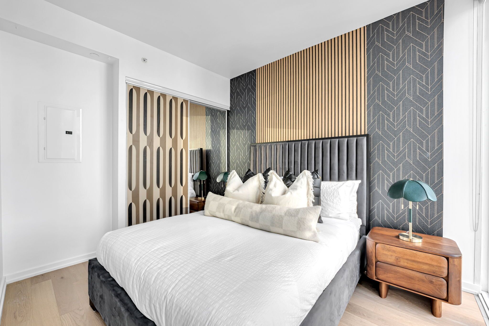 Un dormitorio moderno con una cama grande, una mesita de noche con lámpara y un panel decorativo en la pared.