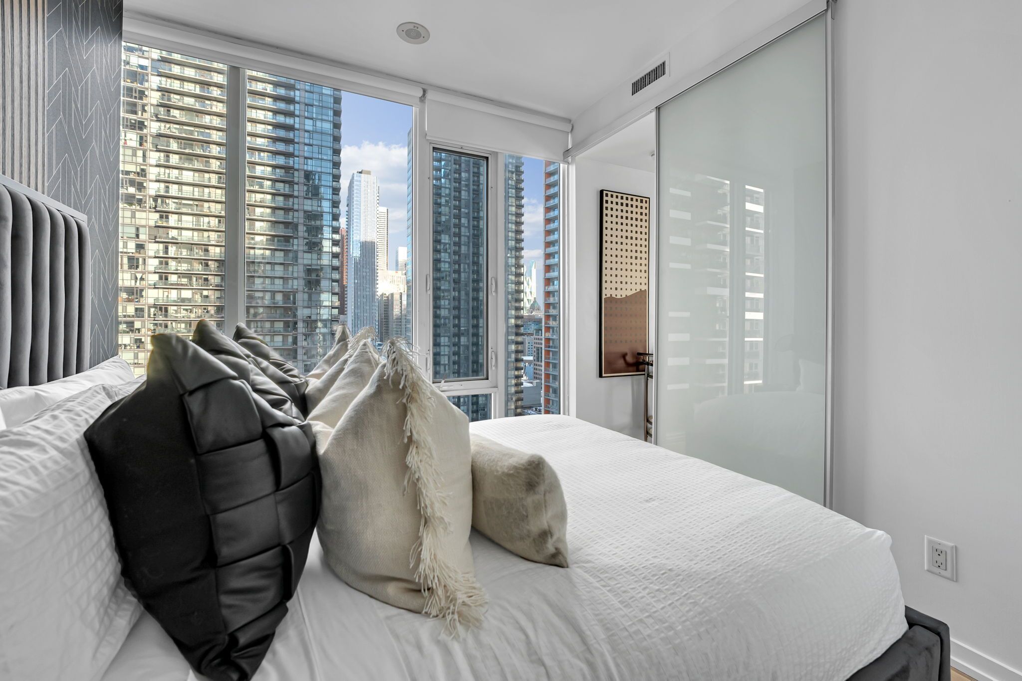 A modern hotel room with a large bed, city views, and a sliding glass door.