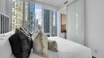A modern hotel room with a large bed, city views, and a sliding glass door.