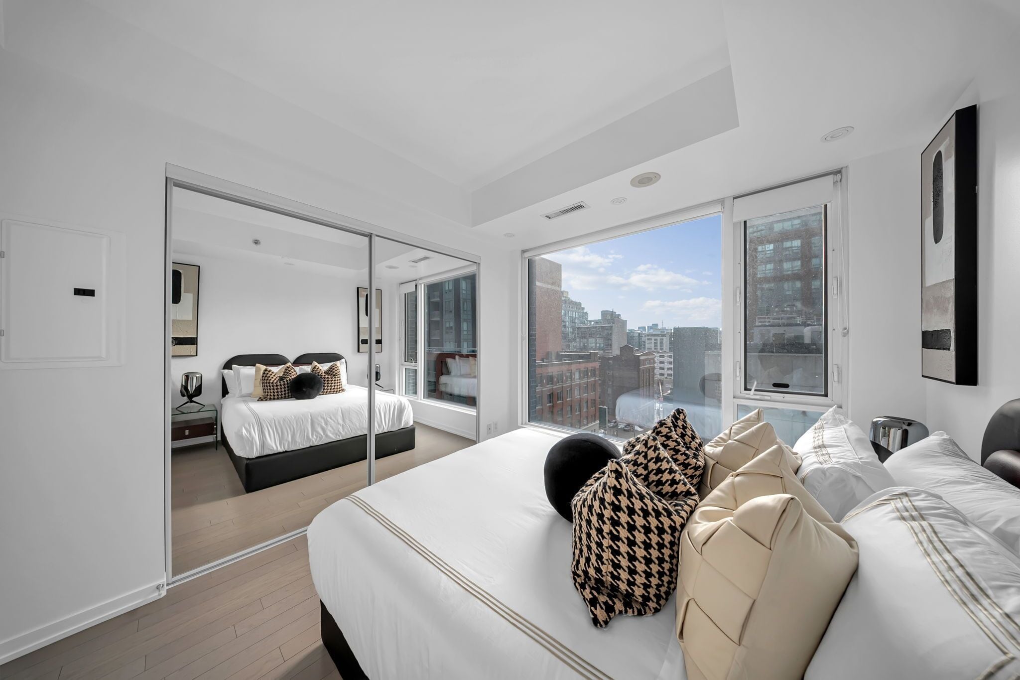 Quarto moderno com uma cama grande, uma cama adicional e vista para a cidade através de amplas janelas.