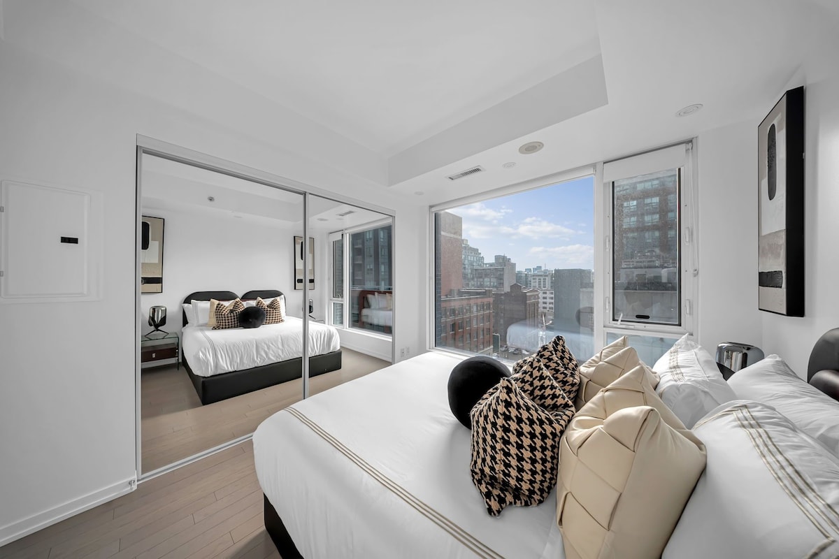 A modern bedroom with a large bed, a second bed, and a city view through large windows.
