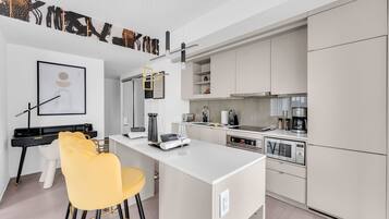 A modern kitchen with white cabinets, a central island, and a dining area with yellow chairs.
