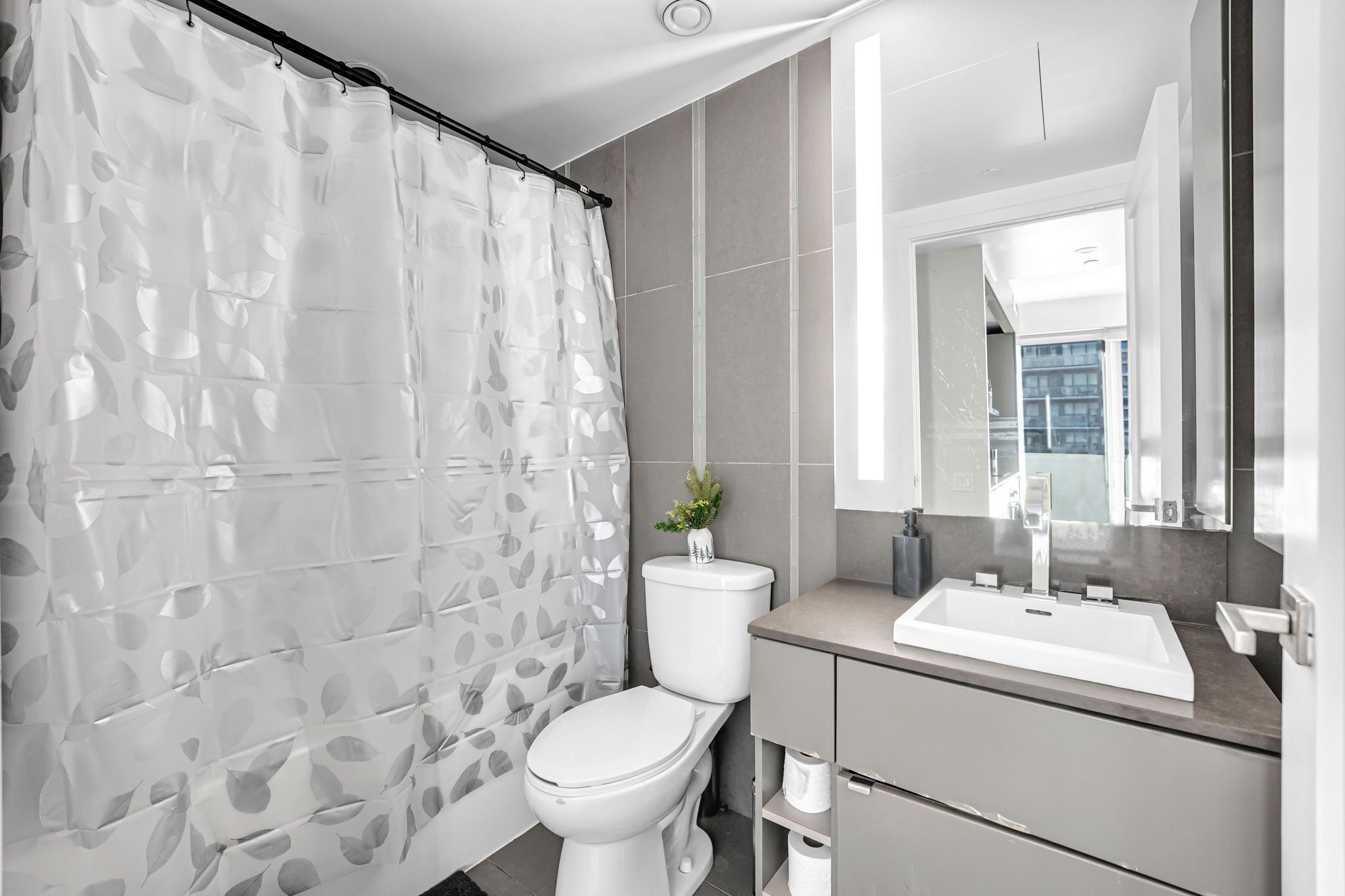 A modern bathroom with a shower curtain, toilet, sink, and mirror.