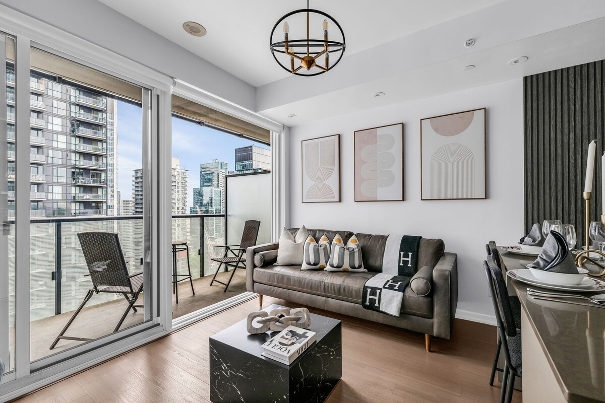 A modern living room with a sofa, a dining table set, a balcony with a chair, and city views.