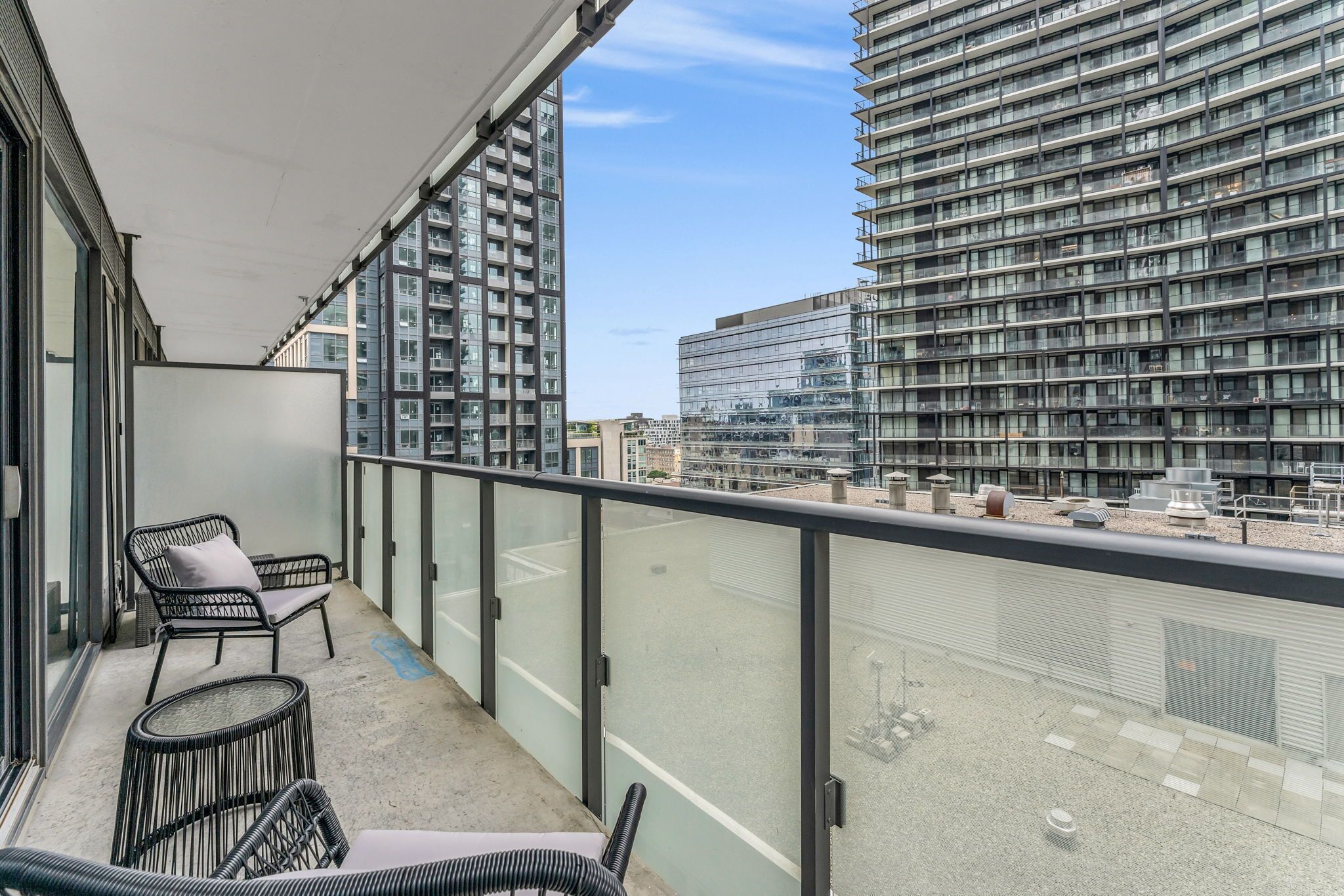 Ein Balkon mit Blick auf hohe Gebäude, einem Stuhl und einem kleinen Tisch.