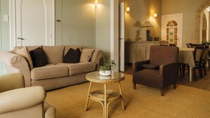 Un salón con un sofá color beige, una mesa de centro redonda de mimbre y un sillón marrón.
