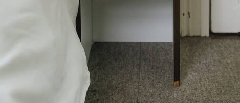 A white bed with a white headboard, a white nightstand with a single shelf, and a closed door.