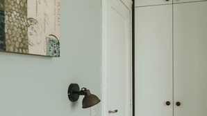Una habitación con un armario blanco, una lámpara de pared y una pequeña mesa blanca.
