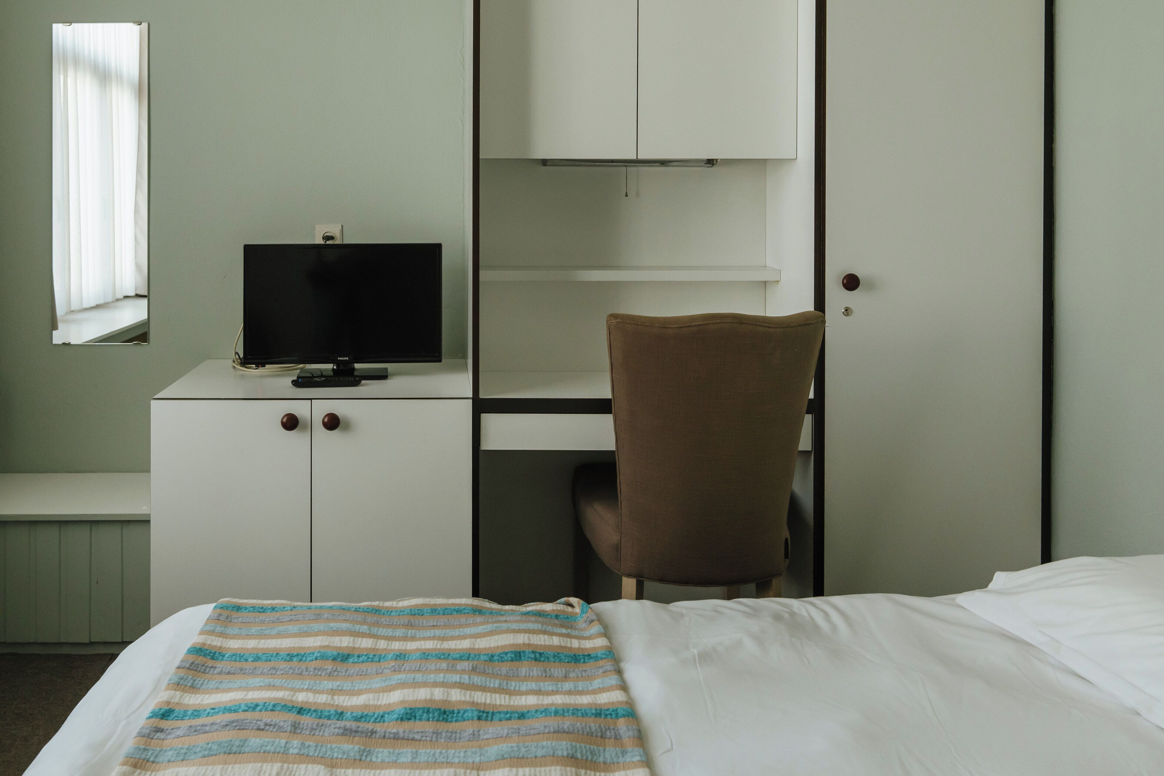 Un dormitorio con cama, escritorio con televisor, silla y armario.