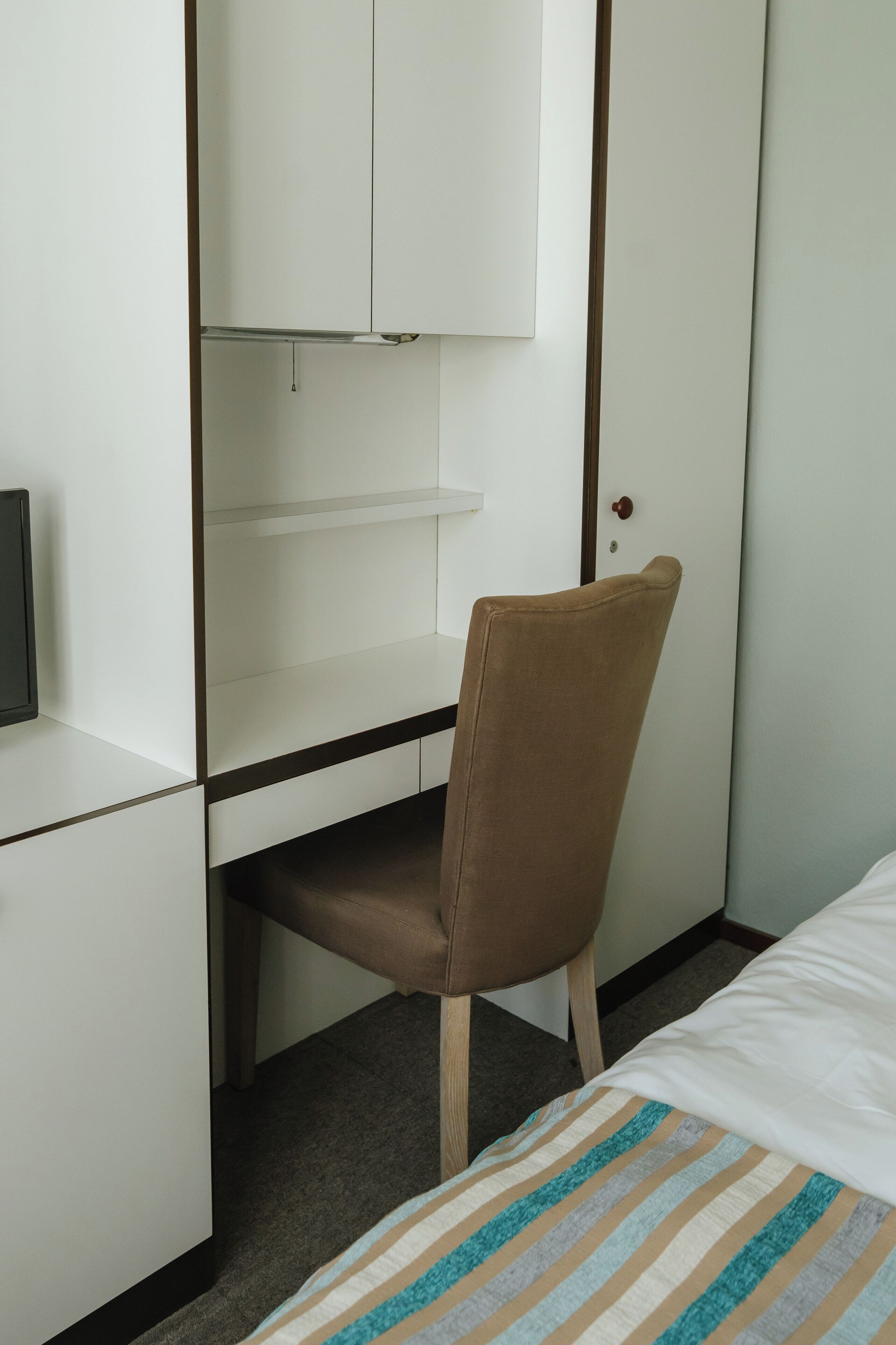 A hotel room with a bed, a desk with a chair, and a wardrobe.