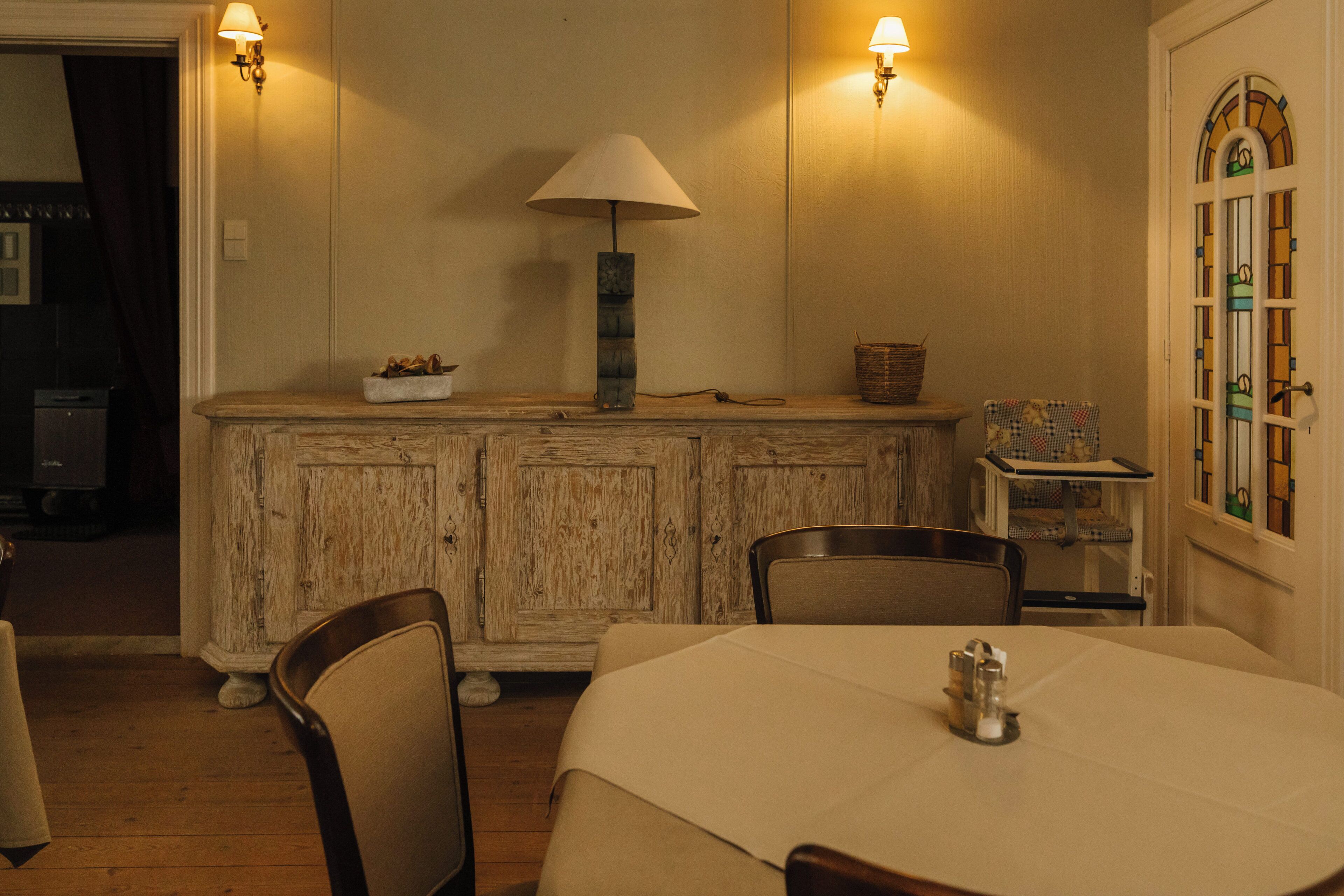 A dining area with a wooden cabinet, a table, chairs, and a lamp.