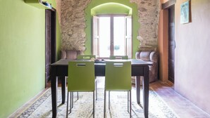 Un área de comedor con una mesa y sillas, un lámpara colgante, una pared de piedra y vistas a través de un arco.