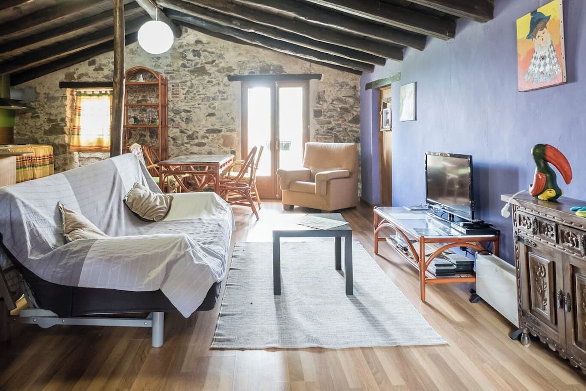 A rustic room with a wooden ceiling, a bed, a TV, and a dining area with chairs and a table.