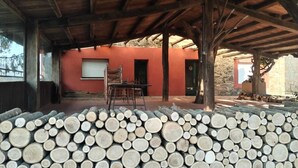 Un espacio cubierto al aire libre con una pila de leña, un edificio rojo y una mesa de metal.