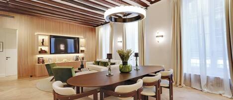 Un salon moderne avec un plafond en bois, un grand téléviseur à écran plat, une table à manger avec des chaises et un canapé.