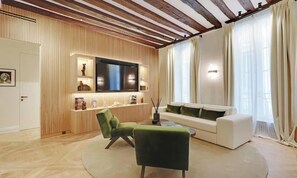 A modern living room with a flat-screen TV, a sofa, and two armchairs.