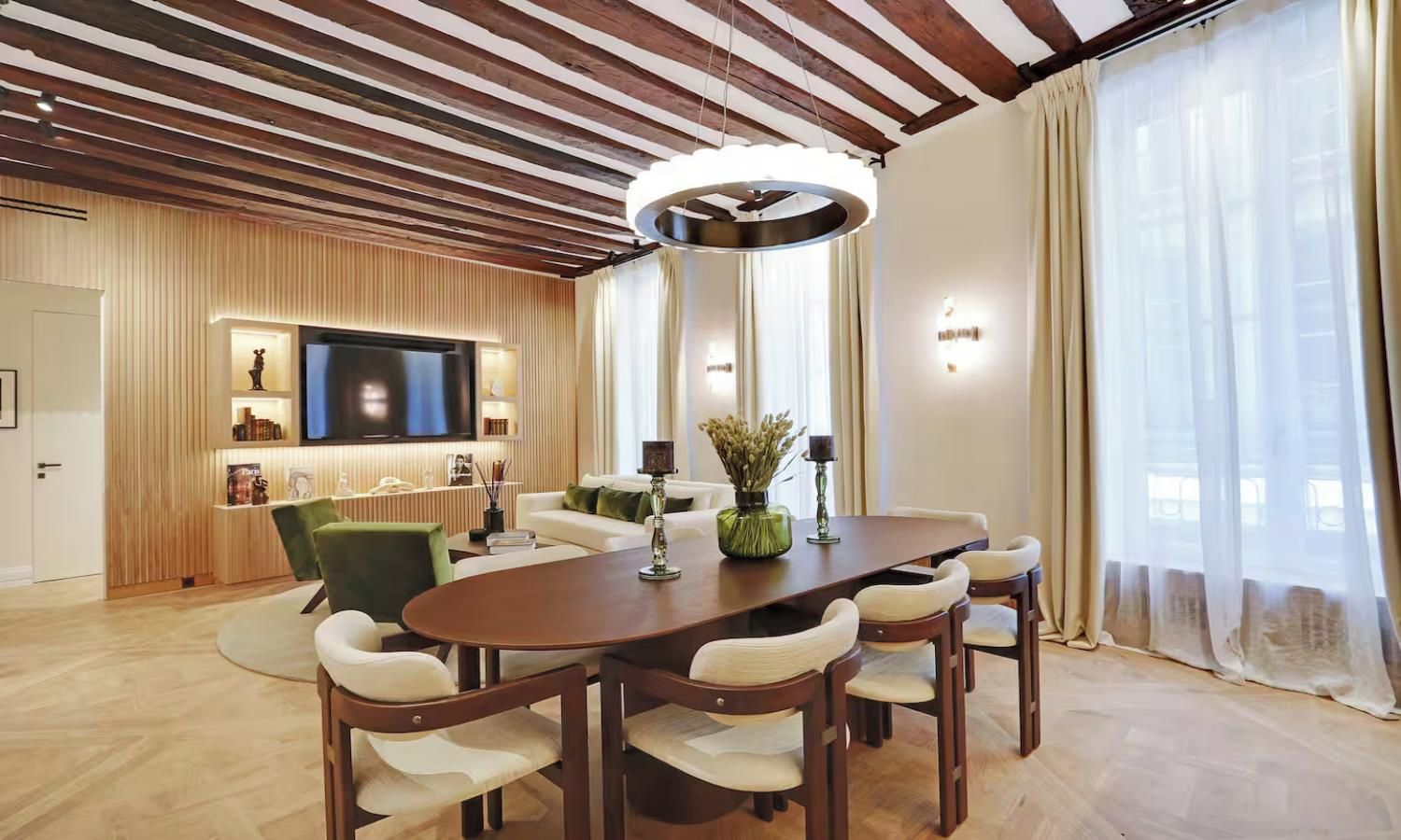 A modern living room with a wooden ceiling, a flat-screen TV, a dining table with chairs, and a sofa.