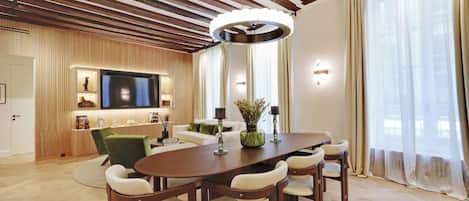 A modern living room with a wooden ceiling, a flat-screen TV, a dining table with chairs, and a sofa.